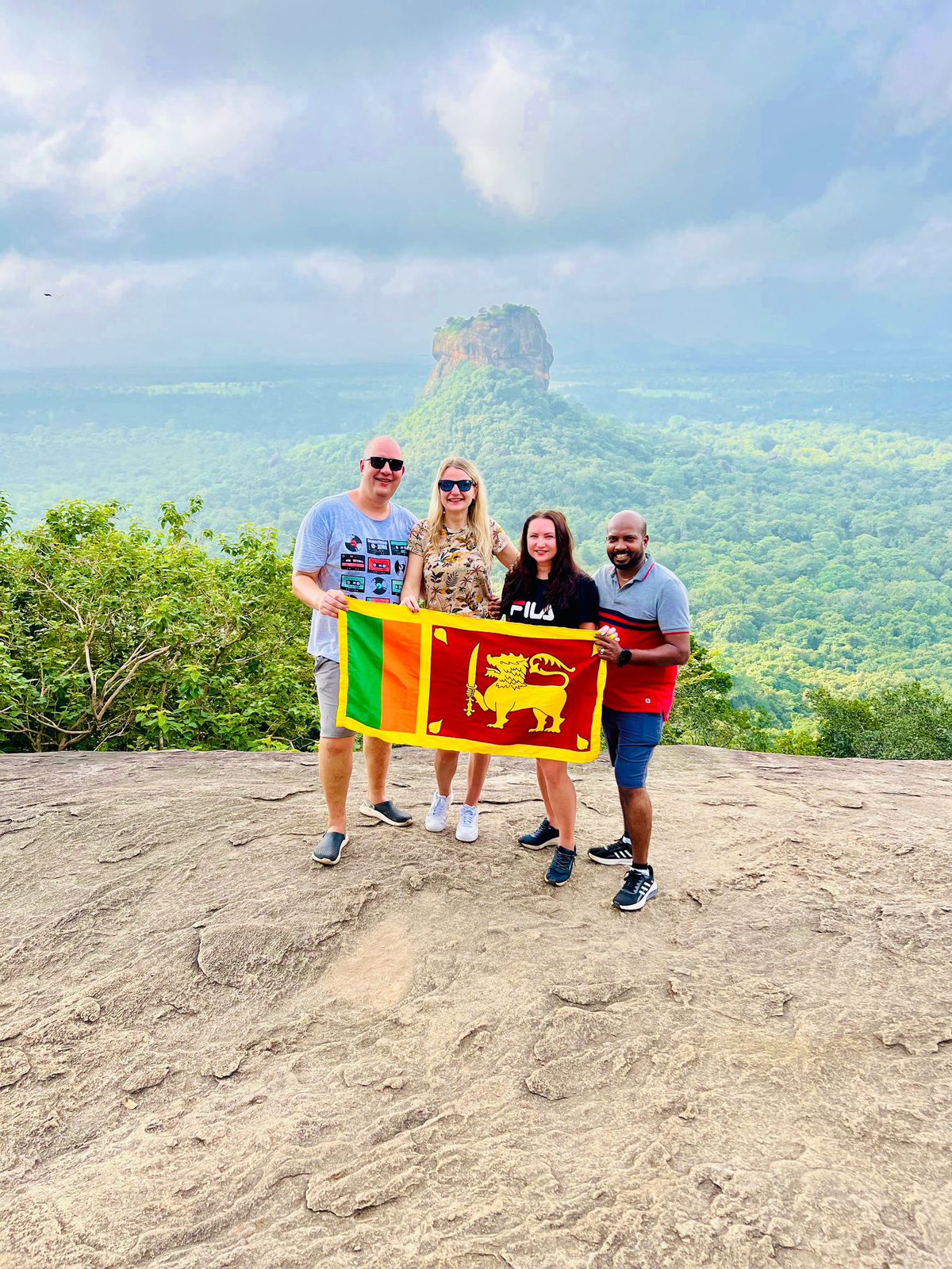 A group holding a Sri Lankan flag at a rocky viewpoint