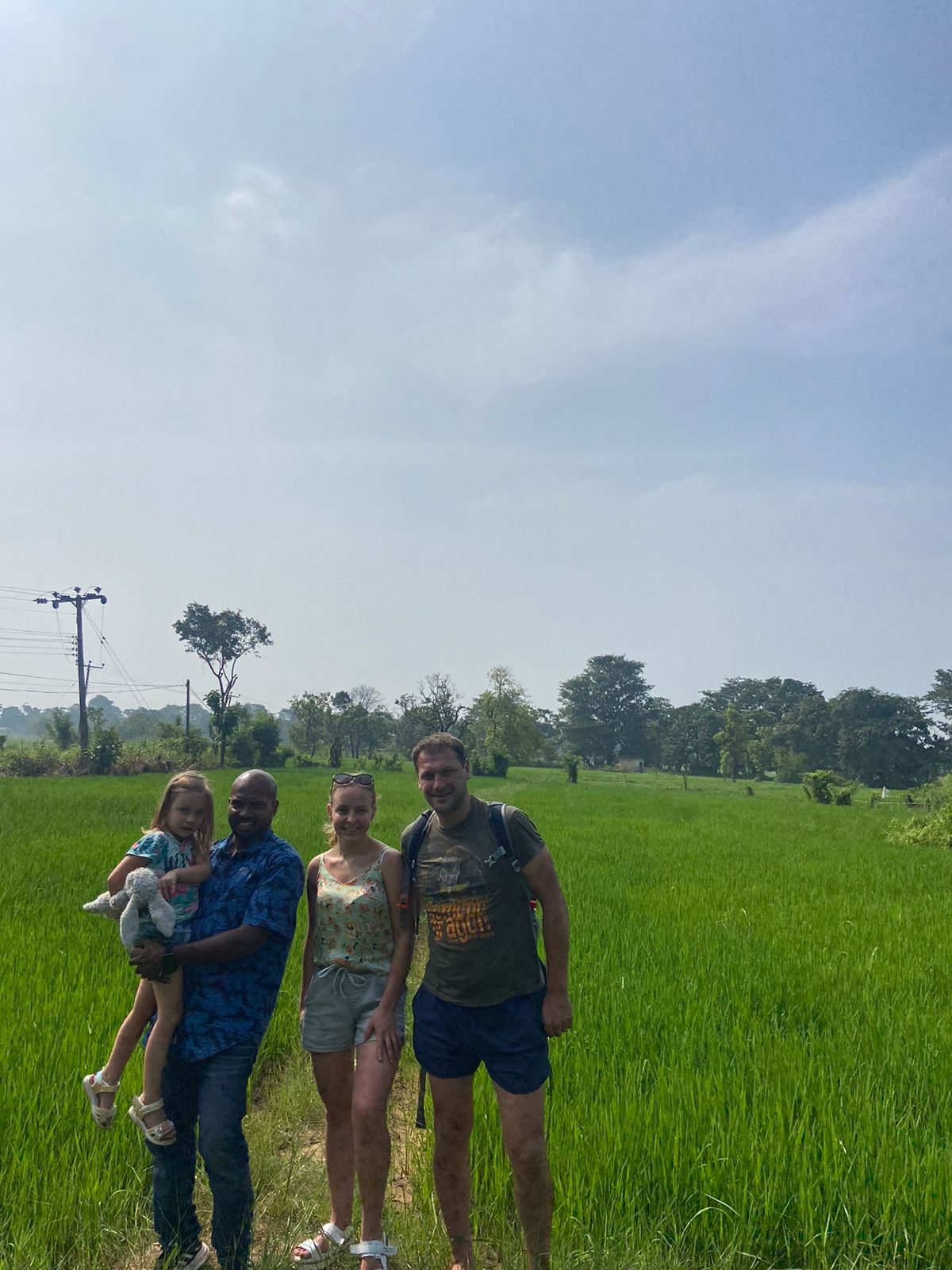 Three visitors standing beside a green rice field