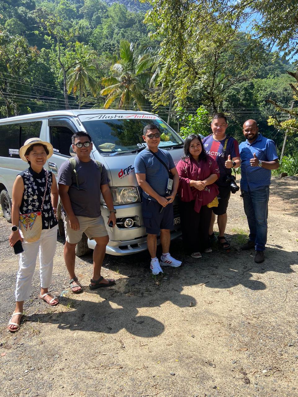 A group standing beside a tour van under palm trees