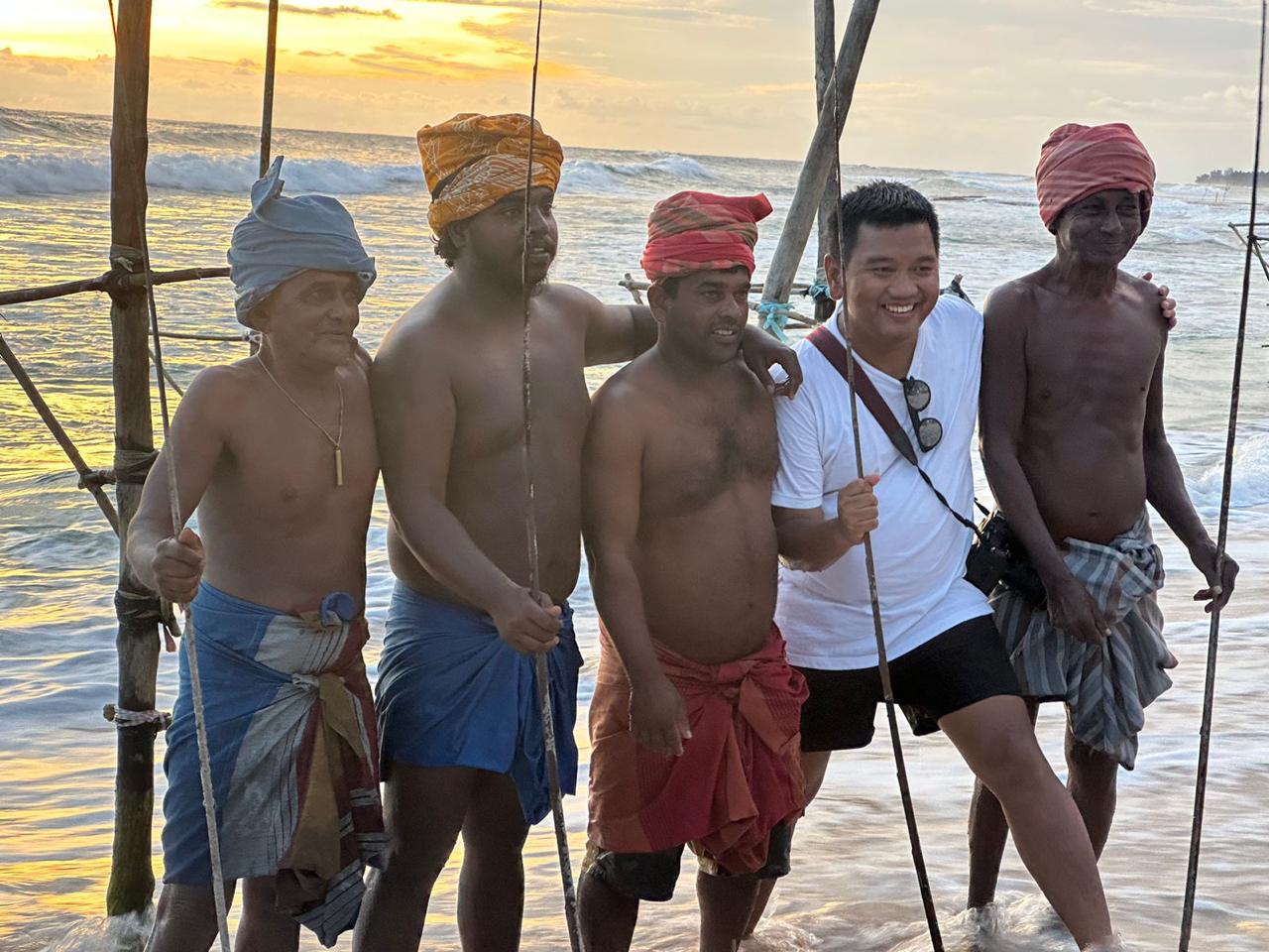 A visitor meeting stilt fishermen by the sea at sunset