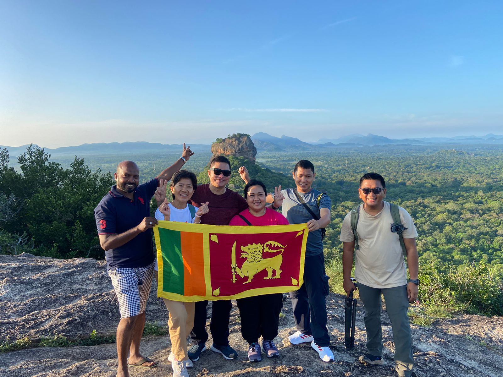 A group holding a Sri Lankan flag above a forest landscape